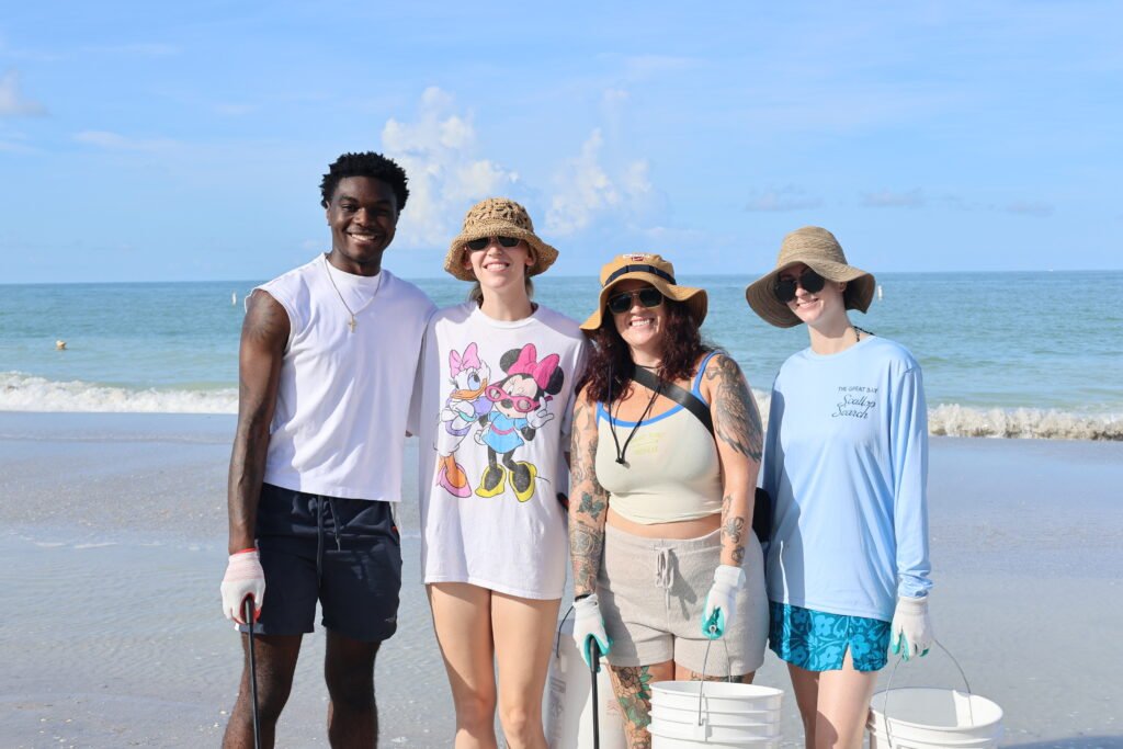 Volunteers smiling on Madeira Beach during a beach cleanup on a sunny day.