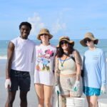 Volunteers smiling on Madeira Beach during a beach cleanup on a sunny day.