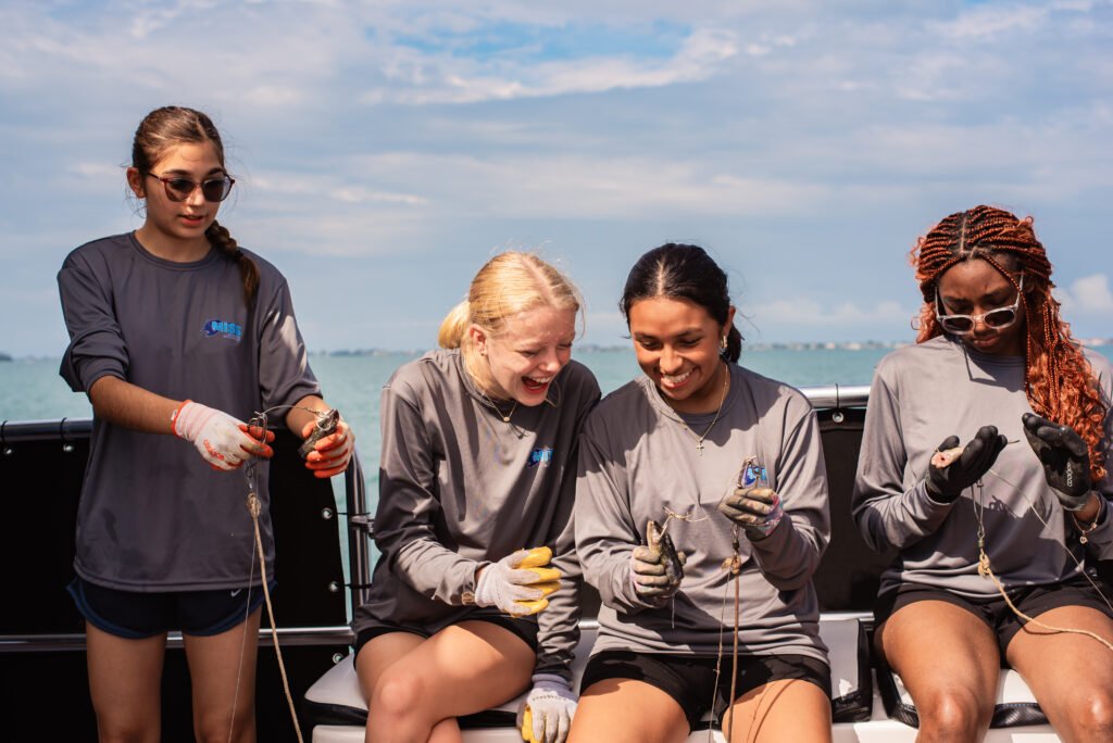 Four students laugh together while hooking bait on a research boat during a shark science trip with Minorities in Shark Science (MISS).
