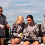 Four students laugh together while hooking bait on a research boat during a shark science trip with Minorities in Shark Science (MISS).